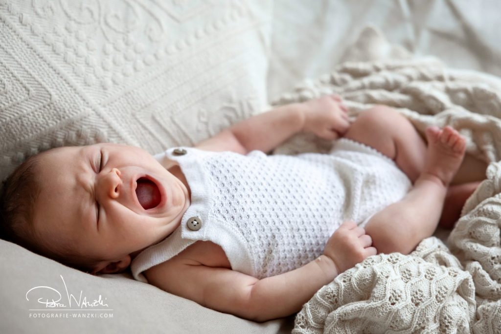 Newborn Fotoshootings Winterthur, gähnendes Baby, eingewickelt in kuschelige Decke, helle Farben, herzig