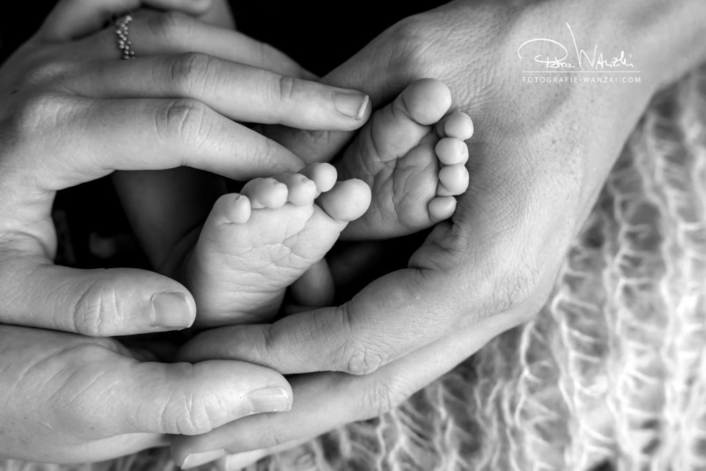 Babyfoto zuhause von Babyfüssen. Werden von den Eltern liebevoll gehalten, Bild in schwarz-weiss, kuschelige Decke im Hintergrund