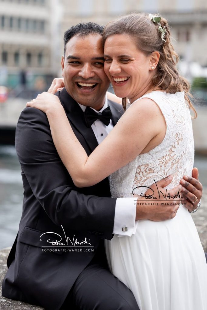 Hochzeitsbild mit Brautpaar, das sich umarmt und lacht, sie sind in Zürich an der Limmat, fotografiert von Fotografie Wanzki aus Winterthur