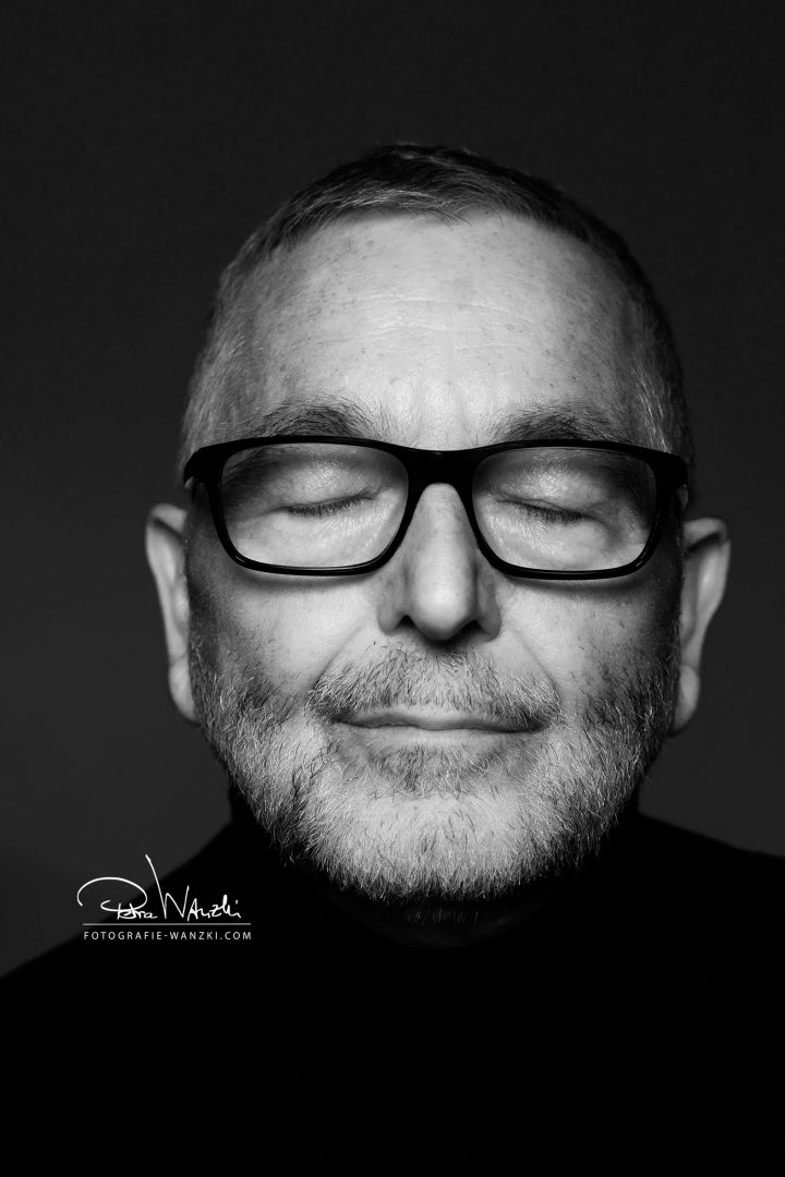 ausdrucksstarkes schwarz-weiss portrait von einem Mann mittleren Alters mit geschlossenen Augen und einer schwarzen Brille.
