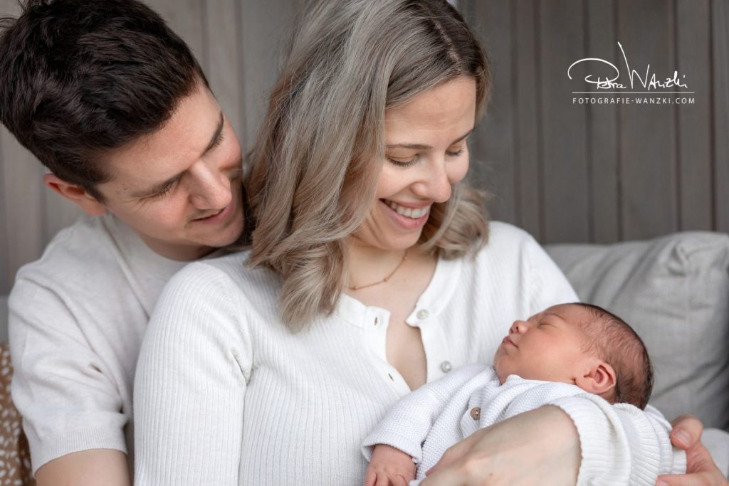 Eltern lachen ihr neugeborenes Baby an, Mutter hält es im Arm beim FotoShooting im Thurgau