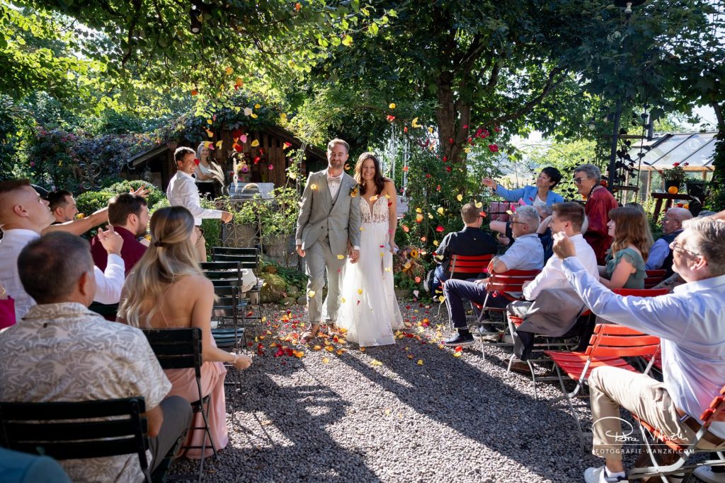 Hochzeitsfotograf, Brautpaar wird mit Rosenblättern beglückwünscht, im grünen Garten vom "Am Charrewäg" bei Effretikon Illnau, mit Gästen, die auf roten Stühlen sitzen