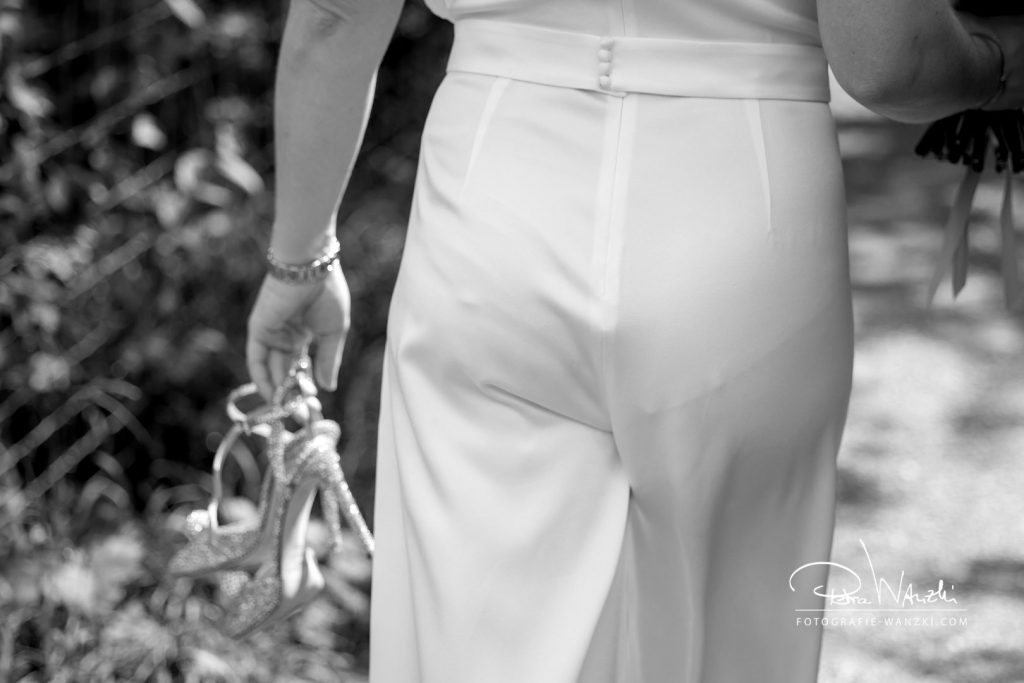 Moderne Braut im Hosenanzug, Brautschuhe von Jimmy Choo in der Hand haltend