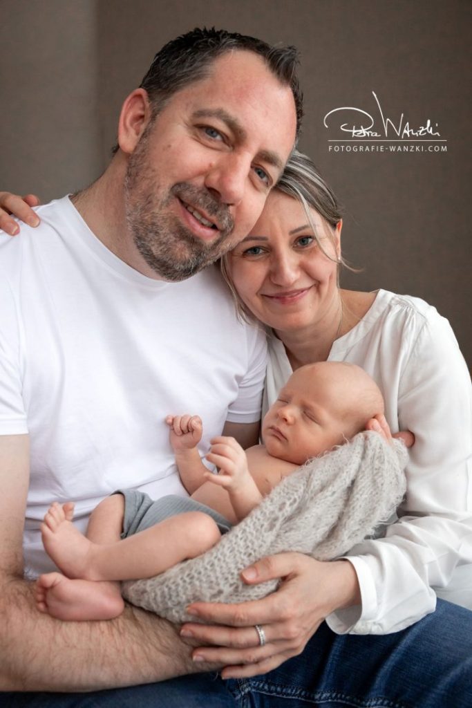 Familienbild mit Neugeborenem Babys, Vater hält das Baby im Arm, die Mama umarmt beide, Familienglück Winterthur