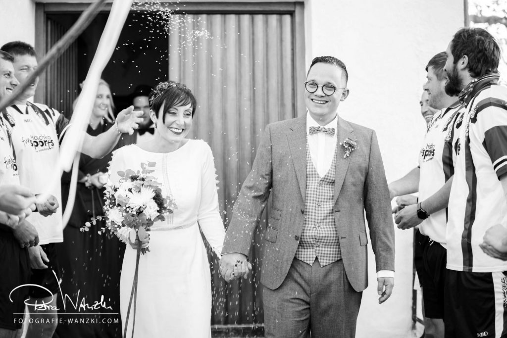 Hochzeitsfotografie – glückliches Brautpaar beim Auszug aus der Kirche nach der Trauung, Gäste stehen Spalier, Bild in schwarz-weiss