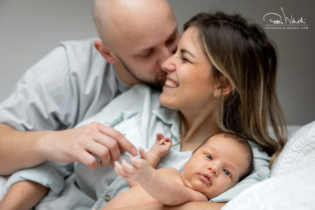Neugeborenes beim Fotoshooting zuhause in Zürich im Arm von Mama, Vater gibt der Mutter einen Kuss, sehr glücklich und emotional