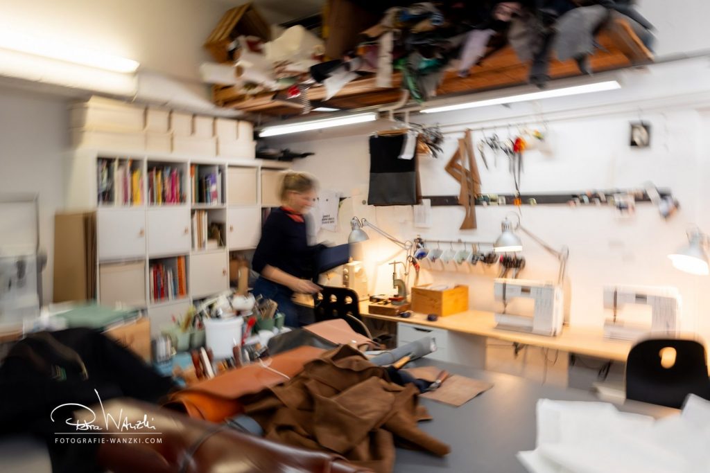 Interieur Atelier in Winterthur, kreatives Chaos, viel Stoff und Leder auf dem Tisch und in den Regalen verteilt, im Hintergrund sind Nähmaschinen erkennbar