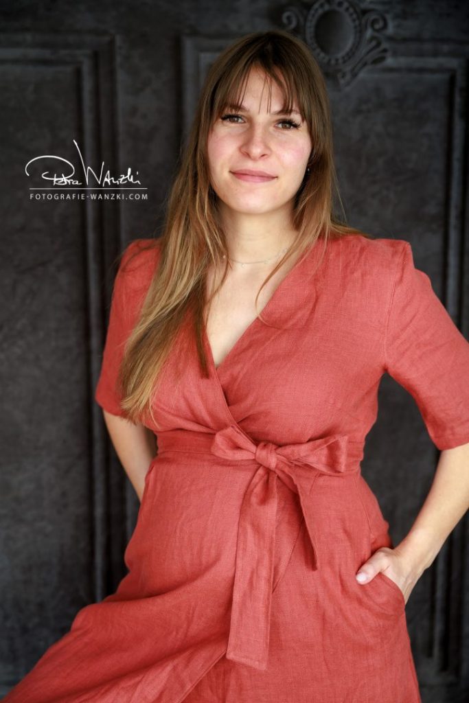 Schwangerschaftskleid für BabyBauch FotoShooting, Frau in kaminrotem Leinenkleid, gewickelt, mit seitlichen Taschen und Schleife um den Babybauch
