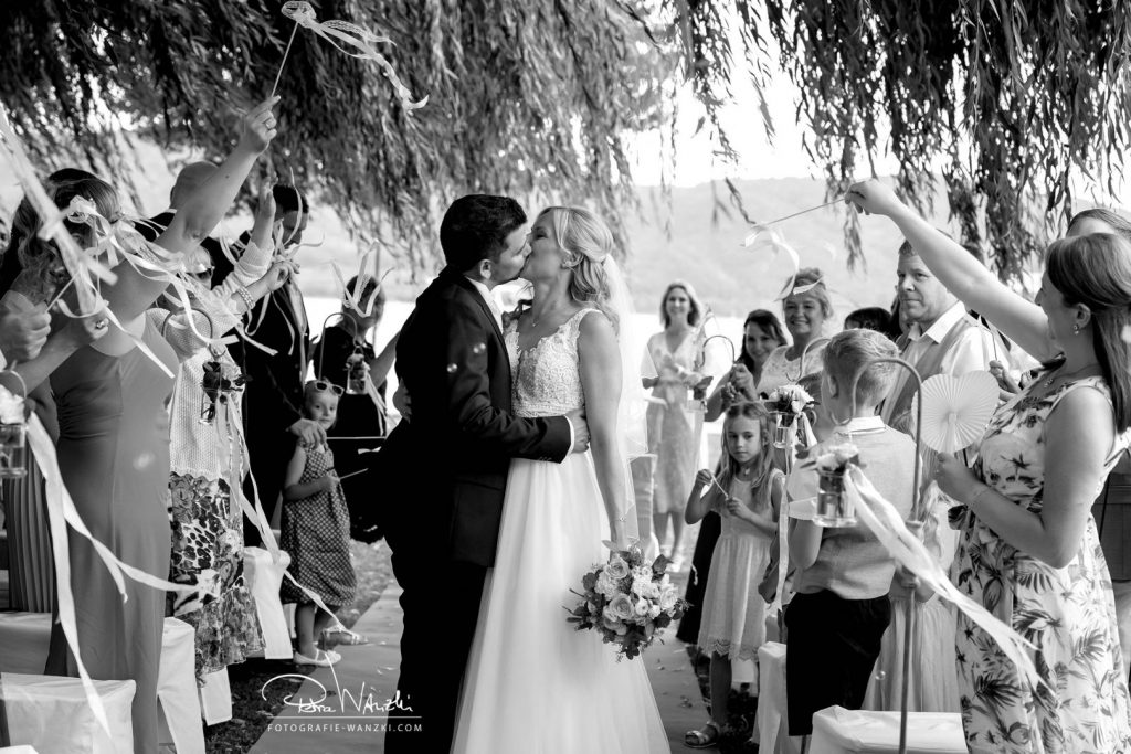 Brautpaar küsst sich bei der freien Trauung im Garten am Bodensee, die Gäste jubeln, Bild in schwarz-weiss