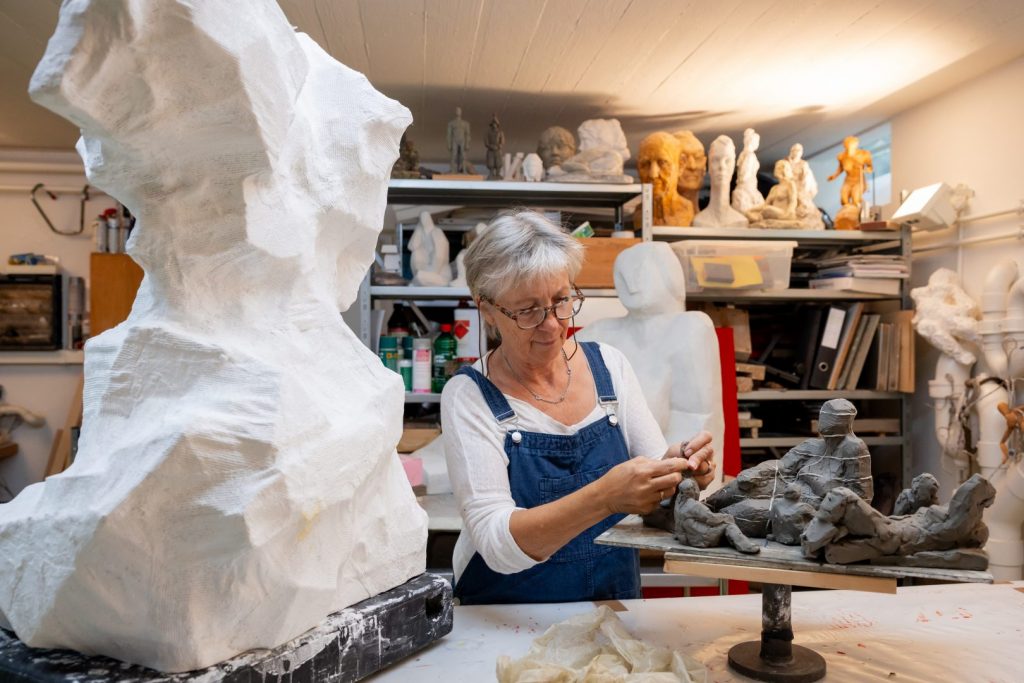 Künstlerportrait in ihrem Atelier in Winterthur, Künstlerin arbeitet an ihren Büsten, im Hintergrund Regale voll mit Kunstwerke