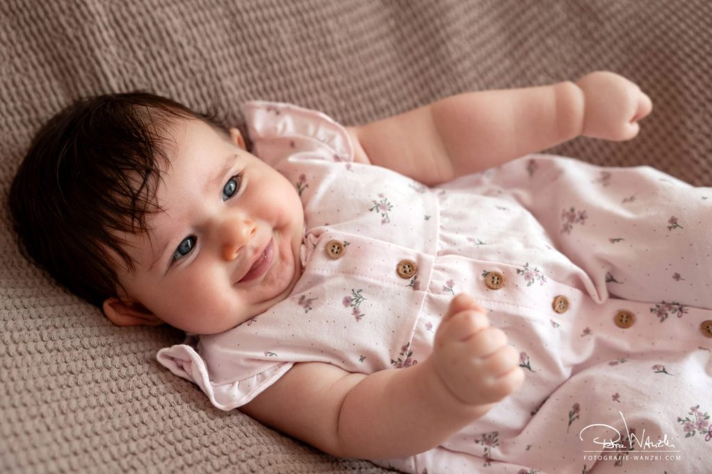 drei Monate Baby lacht beim Familien FotoShooting im Fotostudio in Winterthur, Baby hat viel Haar und ein rosa Kleid an