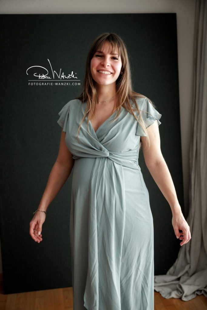 schwangere Frau trägt ein hellblaues Wickelkleid als Outfit beim Schwangerschafts Shooting mit Babybauch im Studio