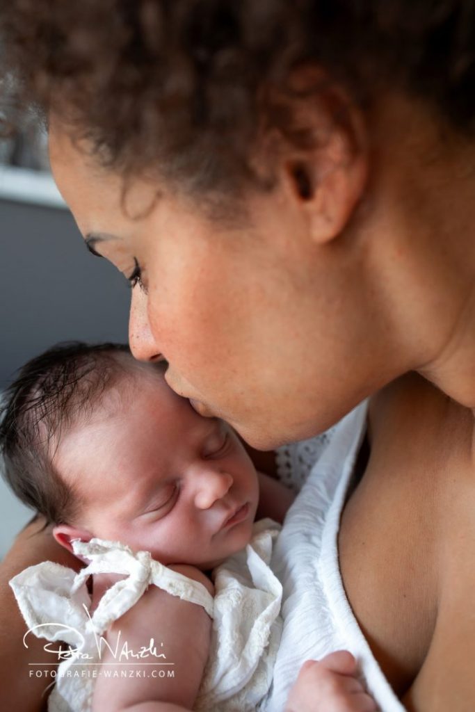 Mutter küsst beim NewbornShooting in Zürich ihre Tochter zärtlich auf den Kopf
