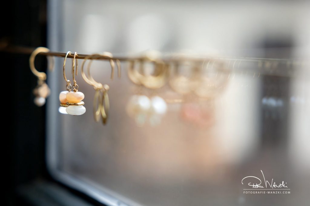 zarter goldener Schmuck Ohrringe in den Farben beige und orange auf einer Stange im Atelier für das Fotoshooting Winterthur aufgereiht, vor einem Fenster fotografiert
