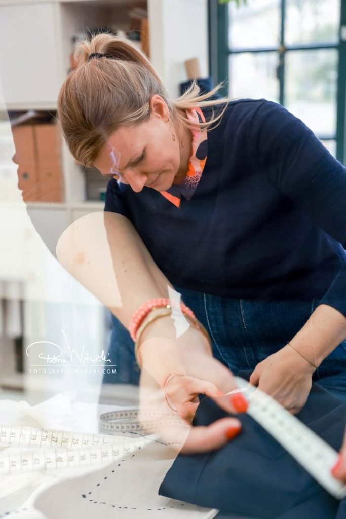 Frau in Jeans gleitet näht mit Massband und Schnittmuster in ihrem Atelier in Winterthur, Doppelbelichtung