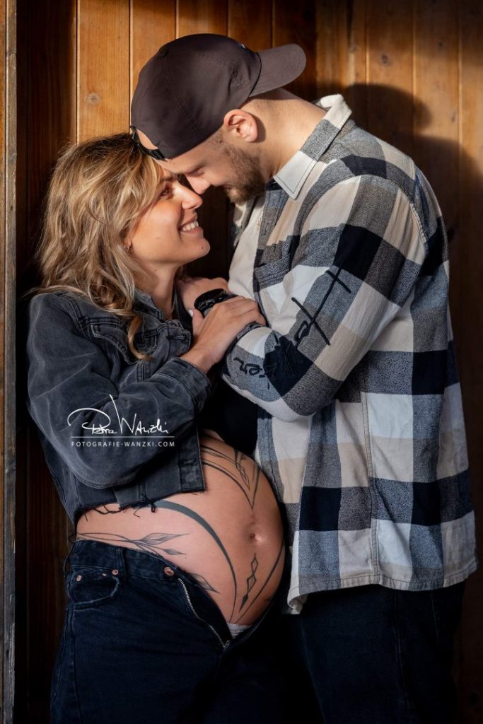 verliebtes Paar lehnt beim FotoShooting Schwangerschaft an einer Holzwand, glücklich, emotional, sehr viel Nähe vom Fotograf Winterthur eingefangen