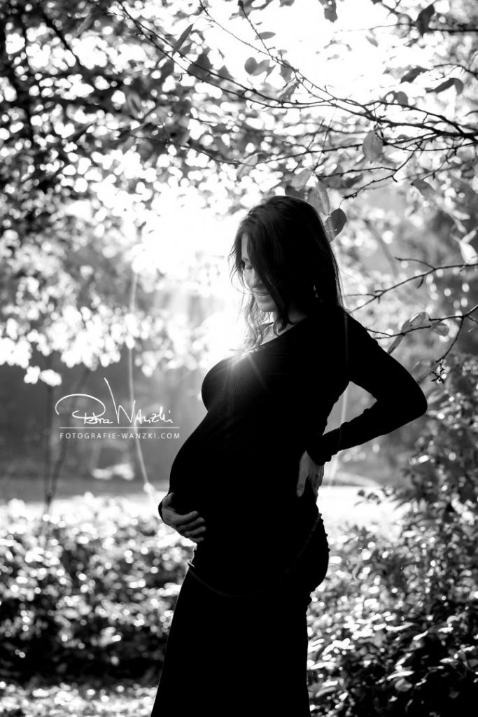 Schwangere Frau beim FotoShooting in Winterthur, im Gegenlicht, unter einem Baum, sie hält sich den Bauch, Bild sehr stimmungsvoll und in schwarz-weis